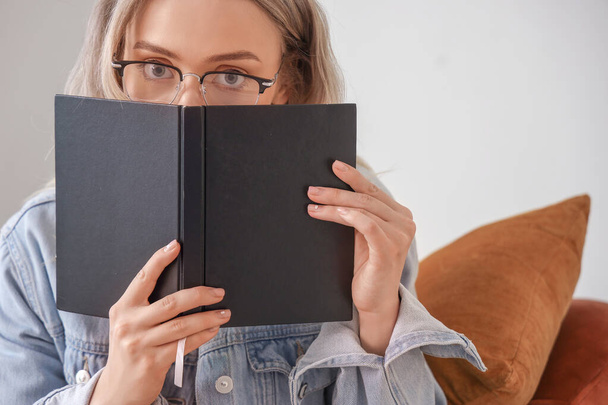 Young woman in stylish eyeglasses reading book at home, closeup - Photo, image