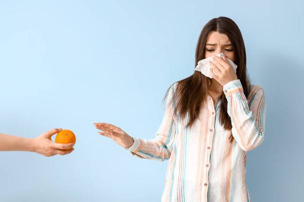 Allergic young woman and female hand with orange on blue background - Foto, immagini