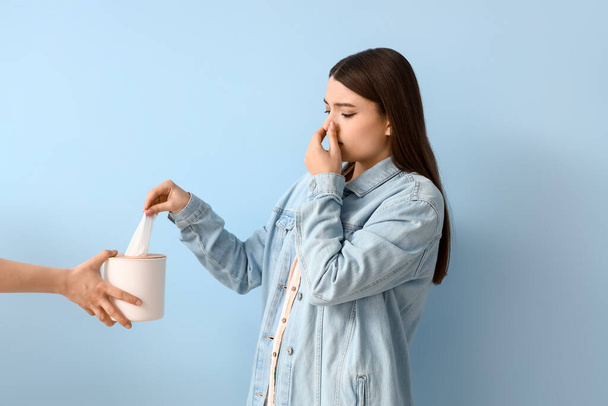 Allergische jonge vrouw neemt weefsel op blauwe achtergrond - Foto, afbeelding