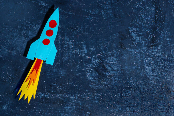 Blue paper rocket on dark grunge background - Фото, изображение