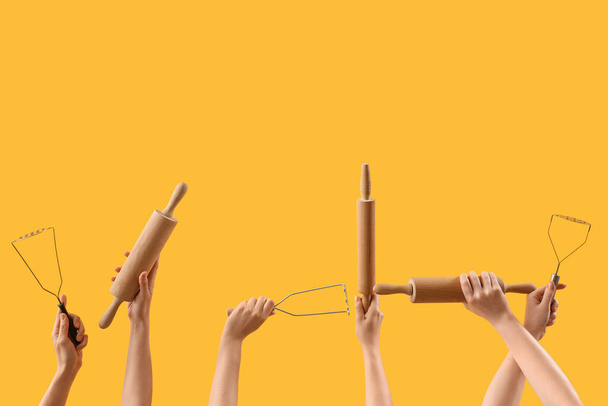 Female hands holding rolling pins and mashers on yellow background - Photo, Image