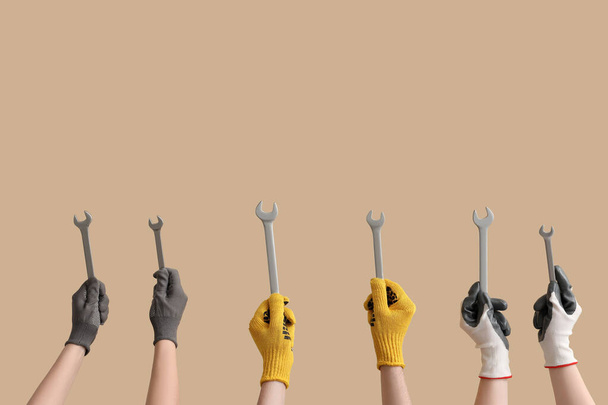 Female and male hands in gloves holding different wrenches on beige background - Foto, Imagem