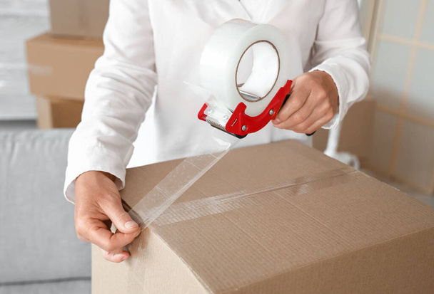 Mature woman taping cardboard box in room on moving day, closeup - Fotoğraf, Görsel