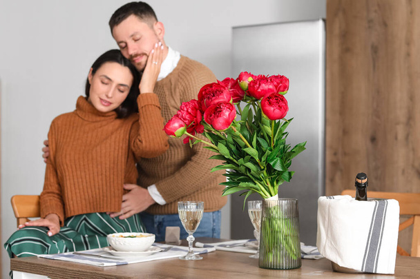 Ваза с цветами и бутылкой вина на столе помолвленной пары на кухне, крупный план - Фото, изображение