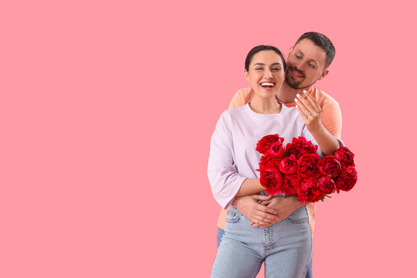 Ευτυχισμένο αρραβωνιασμένο ζευγάρι με λουλούδια αγκαλιασμένο σε ροζ φόντο - Φωτογραφία, εικόνα