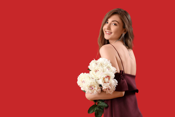 Beautiful young woman with bouquet of peony flowers on red background - 写真・画像