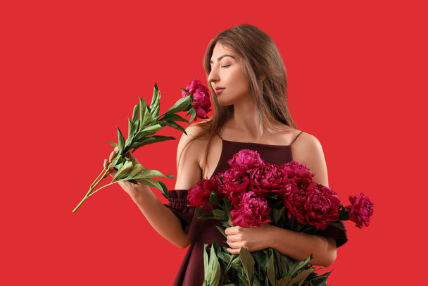 Mooie jonge vrouw met boeket van pioenroos bloemen op rode achtergrond - Foto, afbeelding