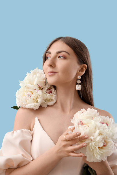 Beautiful young woman with bouquet of peony flowers on blue background - Photo, Image