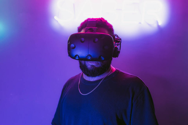 Man in a virtual reality helmet. Neon room with VR games. High quality photo - Фото, изображение