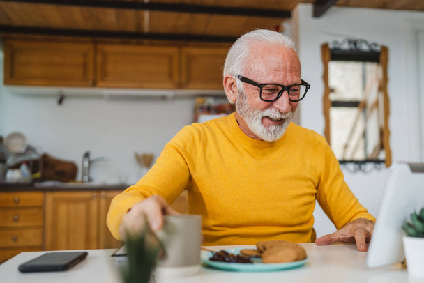 Старший кавказький чоловік використовує цифровий планшет, щоб зробити відеодзвінок вдома
 - Фото, зображення