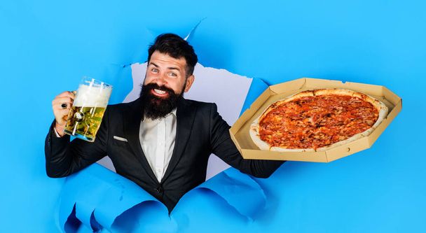 Час піци. Щасливий бородатий чоловік любить смачну піцу і холодне пиво. Швидка їжа. Італійська їжа. Доставка піци. Одягнений у смачну піцу і кухоль пива, що дивиться через паперову яму. Бізнес-обід - Фото, зображення