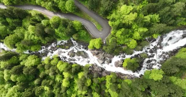Video aereo drone di una vista dall'alto verso il basso su una cascata nelle montagne francesi e una strada asfaltata tortuosa accanto ad essa. - Filmati, video