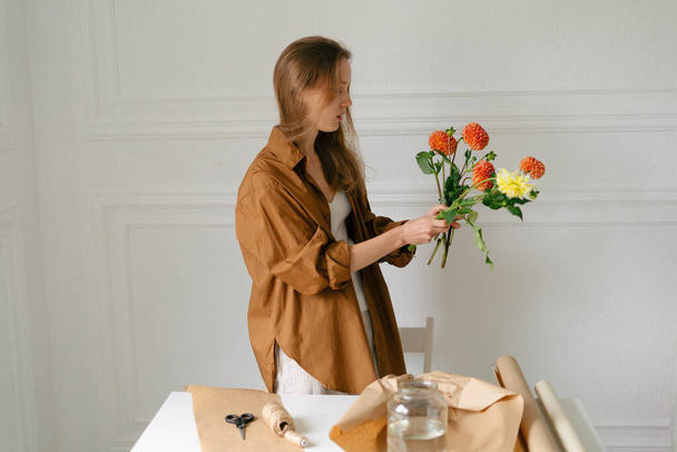 A stylishly dressed female florist collects a bouquet of dahlias on a white background. The concept of small local business and handicrafts - Foto, Imagem