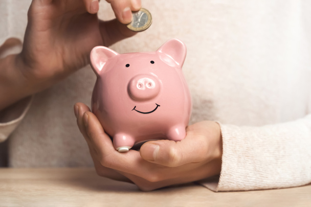 Womens hands carefully hold the piggy bank to preserve wealth, savings and financial success. A girl puts a coin in a piggy bank. - Photo, Image