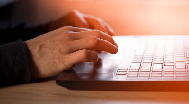 Male hands with a sun effect are typing on a laptop keyboard, close-up view. A man works in an office, is engaged in the development of his business at home, writes messages online. - Foto, Imagem