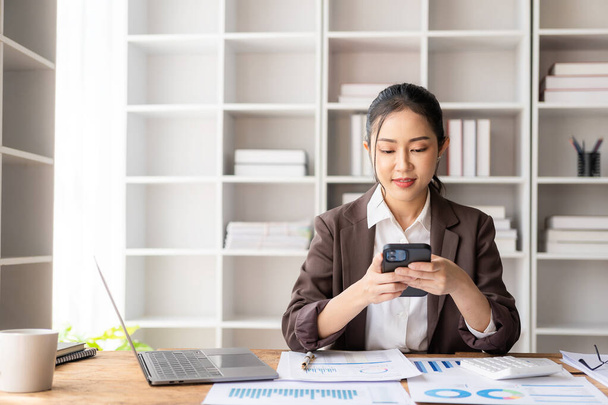 Привлекательная азиатская женщина-бухгалтер в формальном костюме, рассчитывающая кассовый чек и баланс, работающая с компанией ноутбуков ежеквартальная бухгалтерская отчетность - Фото, изображение
