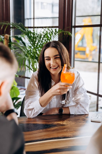 Młoda uśmiechnięta kobieta ciesząca się koktajlem w barze podczas odpoczynku z przyjaciółmi. Uroczystość i koncepcja imprezy - Zdjęcie, obraz