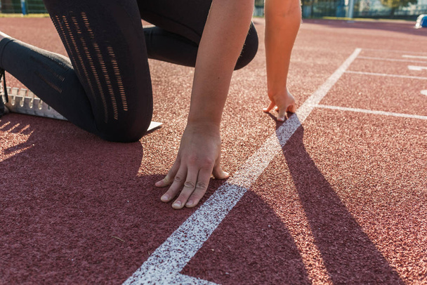 Caucasian woman at the athletic track starting point, hands on the start line and legs on starting block, ready set and go - Φωτογραφία, εικόνα