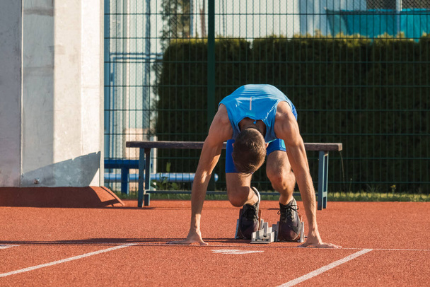 Male Caucasian sprinter assuming a starting position in the starting block during running training at an athletic track, ground level close up shot. - Foto, immagini