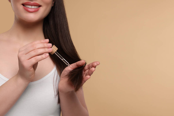 Happy woman applying essential oil onto hair on beige background, closeup and space for text - Foto, Imagen