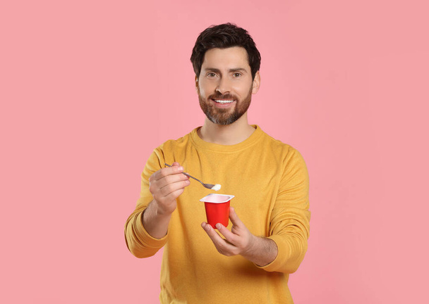 Handsome man with delicious yogurt and spoon on pink background - Zdjęcie, obraz