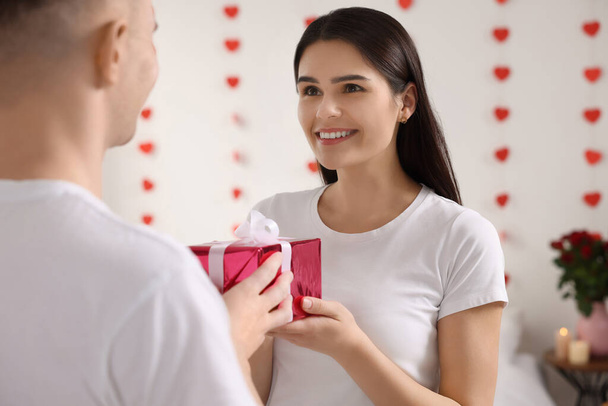 Young woman receiving gift from her boyfriend indoors. Valentine`s day celebration - Foto, Imagen