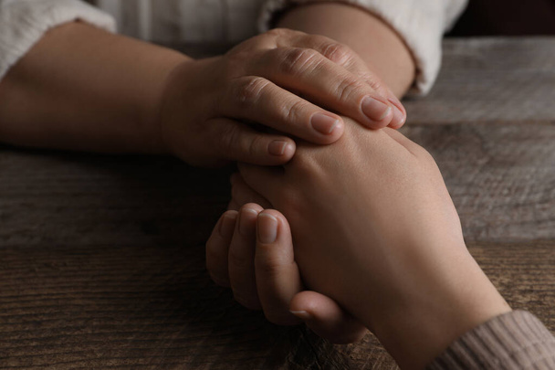 Woman holding hands with her mother at wooden table, closeup - Foto, Imagem