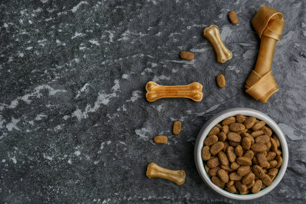 Dry dog food and treats (chew bones) on black textured background, flat lay. Space for text - Foto, imagen