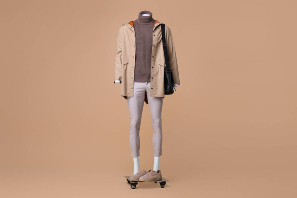 Male mannequin with bag dressed in stylish coat, turtleneck and pants on beige background - Foto, afbeelding