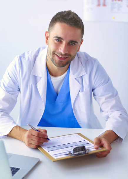 Portrait of a male doctor with laptop sitting at desk in medical office - Photo, image