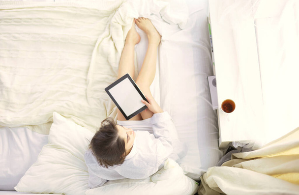 Ritratto di donna che usa tablet e beve caffè seduta sul letto al mattino. - Foto, immagini