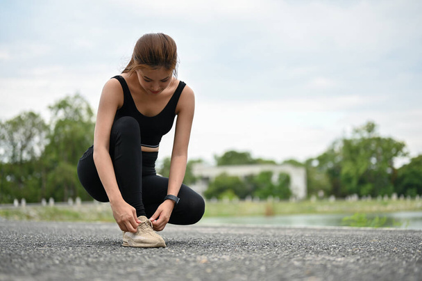 A sporty Asian woman in sportswear tying her running shoelaces on the street at the public park. workout, cardio, training, jogging, running - Foto, immagini