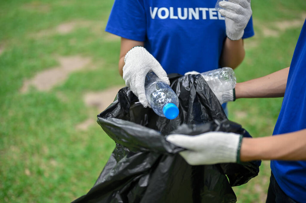 Zbliżenie wizerunku młodych wolontariuszy zbierających śmieci do worka na śmieci i sprzątających wspólnie teren parku publicznego. Wolontariat, wspólnota wsparcia, impreza charytatywna, projekt CSR - Zdjęcie, obraz