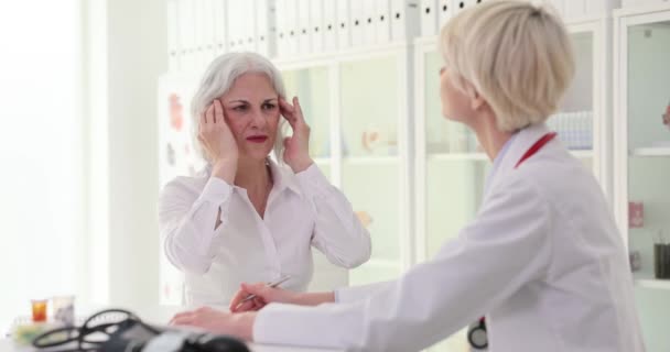 Une belle femme âgée se plaint au médecin d'un mal de tête, d'un gros plan. Soins médicaux à la clinique - Séquence, vidéo
