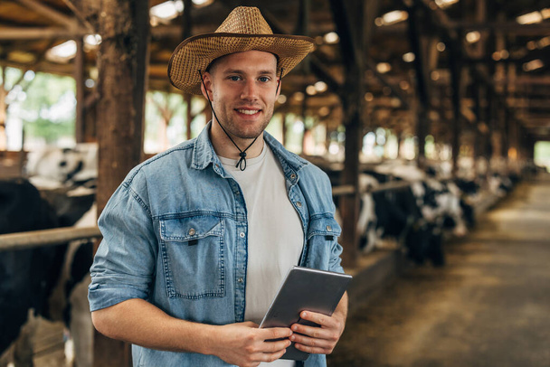 Portrait of a handsome farmer standing in a stable with tablet. - Фото, зображення