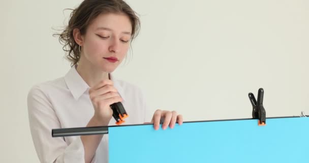 Una mujer en un estudio fotográfico cuelga un tendedero sobre un fondo azul, un primer plano. Sesión de vídeo fotográfico - Metraje, vídeo