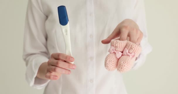 Kobieta trzyma test ciążowy i buty, zbliżenie. Czekając na narodziny dziecka, koncepcja - Materiał filmowy, wideo