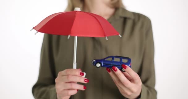 Una donna d'affari tiene un ombrello rosso sopra un'auto giocattolo, un primo piano. Veicolo protetto, assicurazione infortuni - Filmati, video