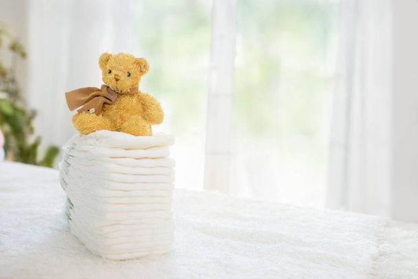 Baby diapers stack cute teddy bear sitting on top. Newborn nappies concept - Fotó, kép