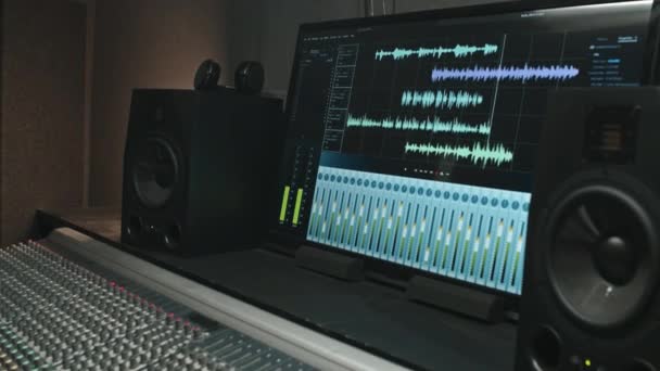 Parte del lugar de trabajo del productor profesional con pantalla que muestra el proceso de grabación con ajustes, ondas de sonido y volumen, dos subwoofers y tablero mezclador - Imágenes, Vídeo