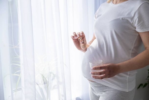 Une femme enceinte boit de l'oméga 3. Concentration sélective. Blanc. - Photo, image