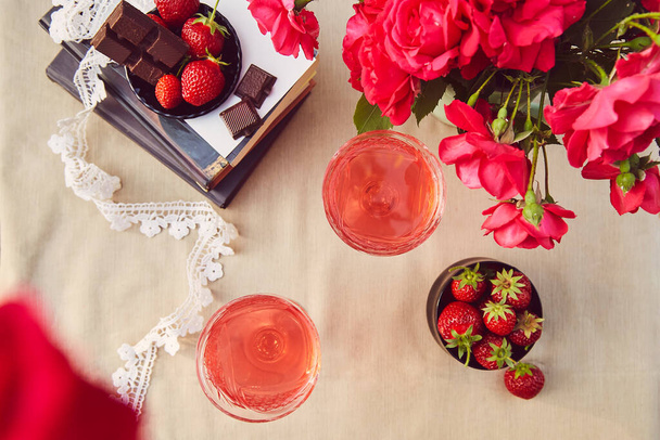 Aesthetics summer table settings. Couple of glasess with red homemade, strawberry infusion. Strawberry and chocolate. Roses bouquet. Flat lay. - Photo, Image
