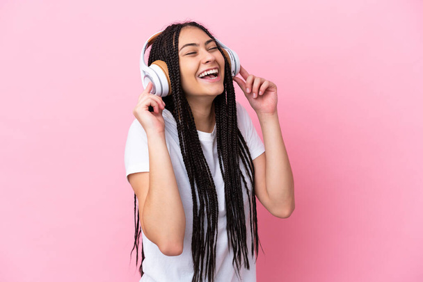 tiener meisje met vlechten over geïsoleerde roze achtergrond luisteren muziek en zingen - Foto, afbeelding