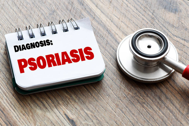 Het woord Psoriasis in een notitieboekje op een houten tafel naast een stethoscoop. - Foto, afbeelding