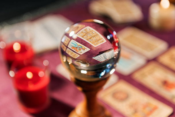 Lasikristallipallon valikoiva painopiste lähellä tarot-kortteja ja kynttilöiden polttaminen pöydällä hämärtynyttä taustaa vasten tulevaisuuden ennustamiseksi - Valokuva, kuva