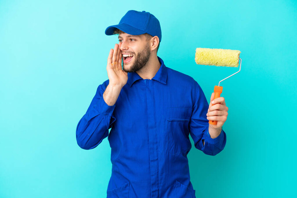 Painter caucasian man isolated on blue background shouting with mouth wide open to the side - Foto, Imagem