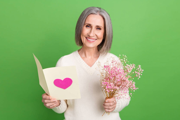 Photo of grey hair retired lady reading greetings congratulations postcard hold bouquet gypsophila isolated on green color background. - Photo, Image