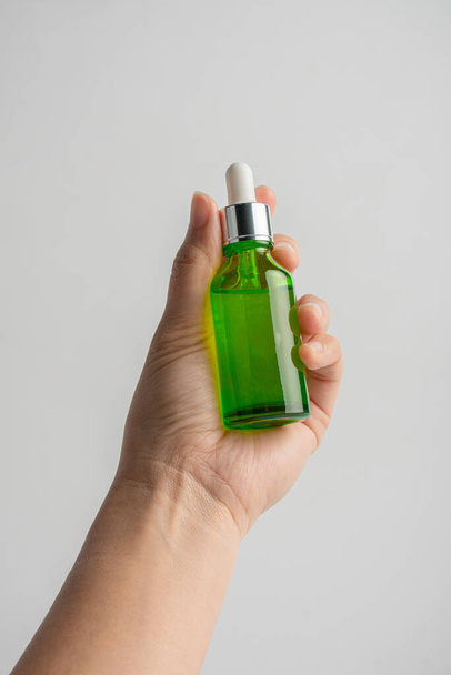 Hand holding up a green glass dropper bottle on white background - Photo, image