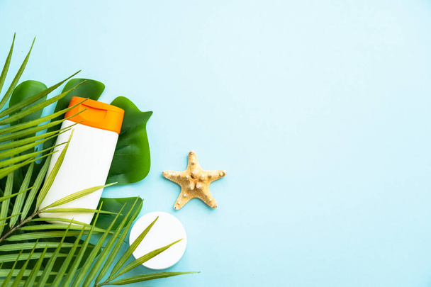 Mavi arka planda palmiye yapraklı güneş kremi ürünleri. Güneş koruması. Metin için alanı olan düz resim. - Fotoğraf, Görsel