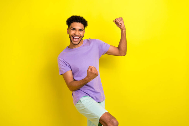 Photo of pretty lucky guy dressed purple t-shirt screaming rising fists isolated yellow color background. - Fotografie, Obrázek